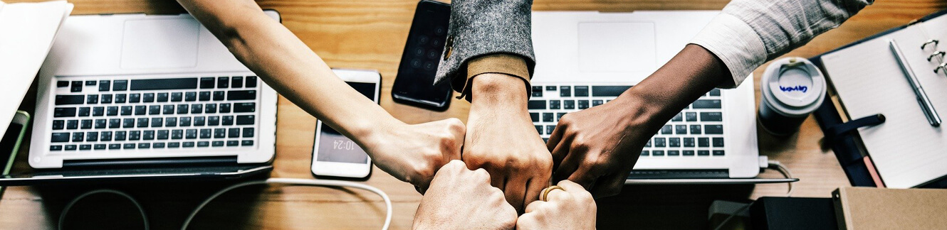 five fists bumping over desk with computers and mobile phone on desk